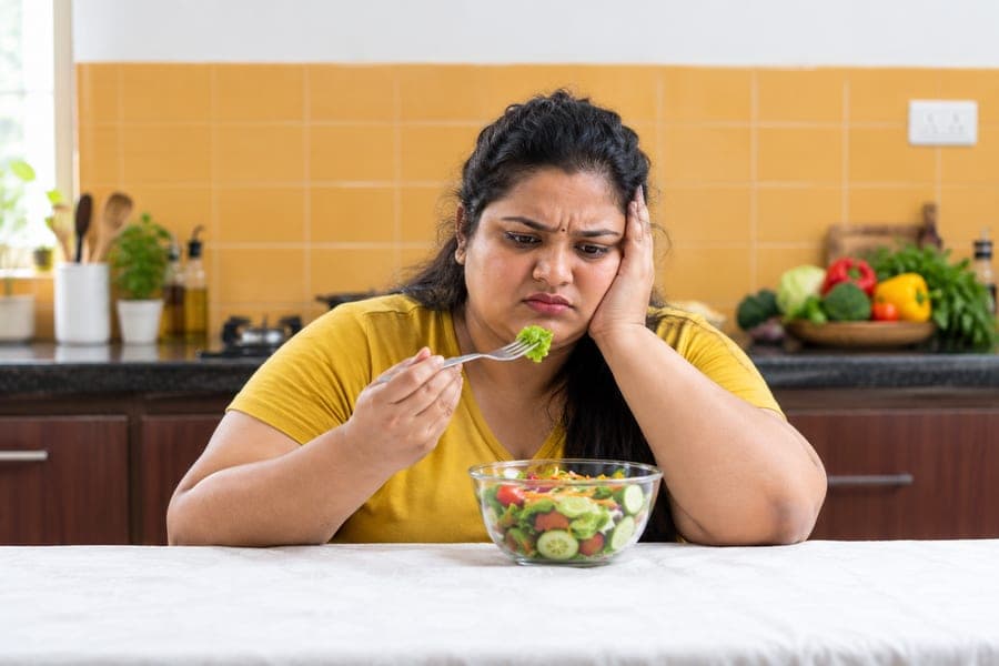 Woman looking unhappily at a bowl of salad
